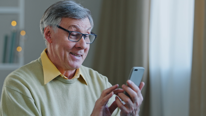 Excited middle aged retired man with glasses holding telephone make online shopping communicates with friends or children using internet app elderly grandpa rejoices successful order learn modern tech | Shutterstock HD Video #1086912869