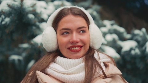Close up portrait young woman with fur earmuffs winter day outdoor. Beautiful caucasian female looking camera and smile