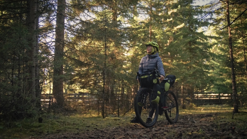 The woman travel on mixed terrain cycle touring with bike bikepacking outdoor. The traveler journey with bicycle bags. Stylish bikepacking, bike, sportswear in green black colors. Magic forest park. Royalty-Free Stock Footage #1086923096