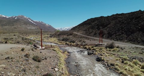 Woman crossing a suspension bridge over a river in Mendoza  With the mountains in the background  the drone goes backwards 