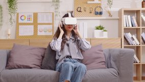 Asian woman using VR virtual reality glasses headset pointing at objects in metaverse. Young woman goggle using VR enjoy at home exciting playing watching 360 degree at home.Virtual Reality Metaverse