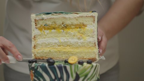 Holding half of cake decorated with mango, passion fruit and blueberry in slow motion. Big cake of 4 layers and cream.