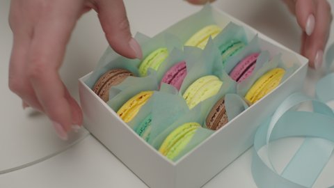 Confectioners hands packing macaron cookies into gift box. Sweet present. Close up, slow motion.