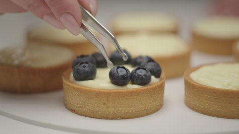 Decorating tarts with blueberries in slow motion, close up. Baking process, confectionery making.