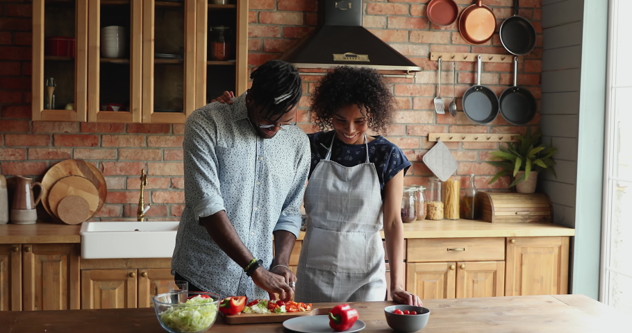 Family portrait of bonding loving married Black couple preparing healthy delicious romantic dinner for two at modern kitchen. Happy spouses homeowners enjoy cooking cutting vegetarian salad together Royalty-Free Stock Footage #1086926576