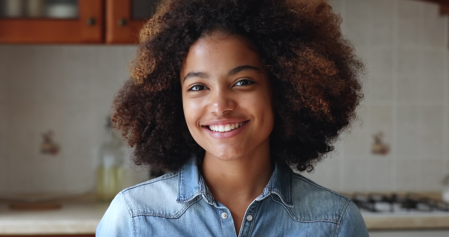 Close up head shot beautiful African teenage girl standing alone in home kitchen smile look at camera, having wide toothy charming smile, natural afro curly hairs poses indoors. Gen Z portrait concept Royalty-Free Stock Footage #1086926591