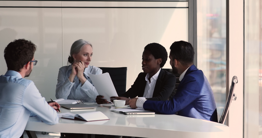 Multiethnic business team senior lady boss diverse young employees have fun at workplace confer sales stats on briefing at boardroom. Laughing businesspeople enjoy funny work moment discussing report Royalty-Free Stock Footage #1086926603