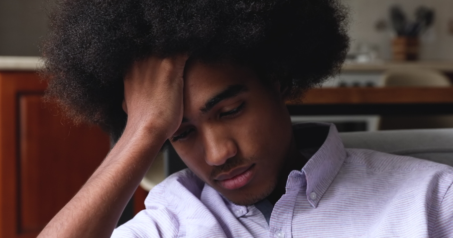 Close up face sad African teenage 18s guy sit at home alone, looks pensive thinks over life concerns or unrequited love, suffers from unfair situation. Teen relation problem, break up, worries concept Royalty-Free Stock Footage #1086926750