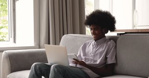 Teenage African adolescent guy studying together with mate through video conference, sit on sofa wear headphones talk to online teacher, prepare for college admission, university exam. Tuition concept