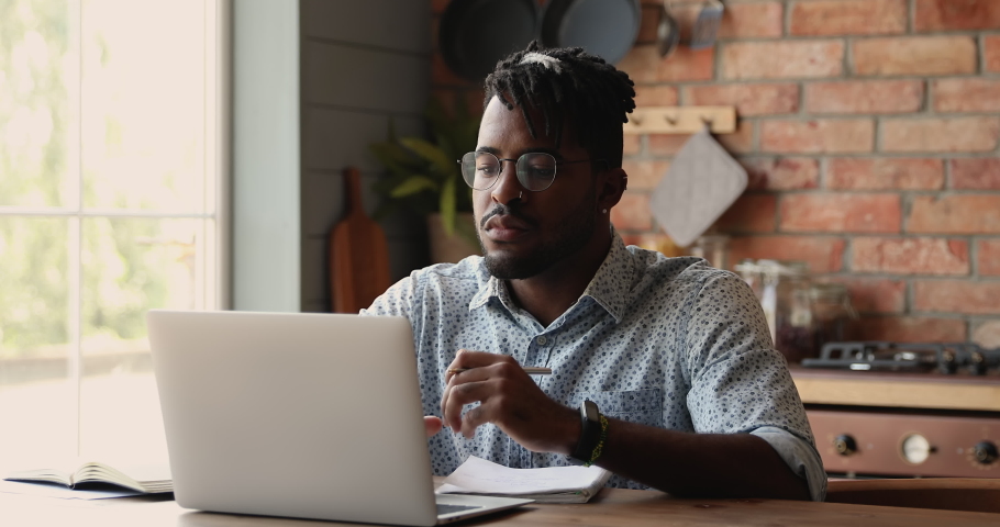 Black man remote student watch web training class webinar on laptop online study new information make brief notes. Young hipster guy sit by pc at home kitchen improve professional skills via elearning Royalty-Free Stock Footage #1086926978