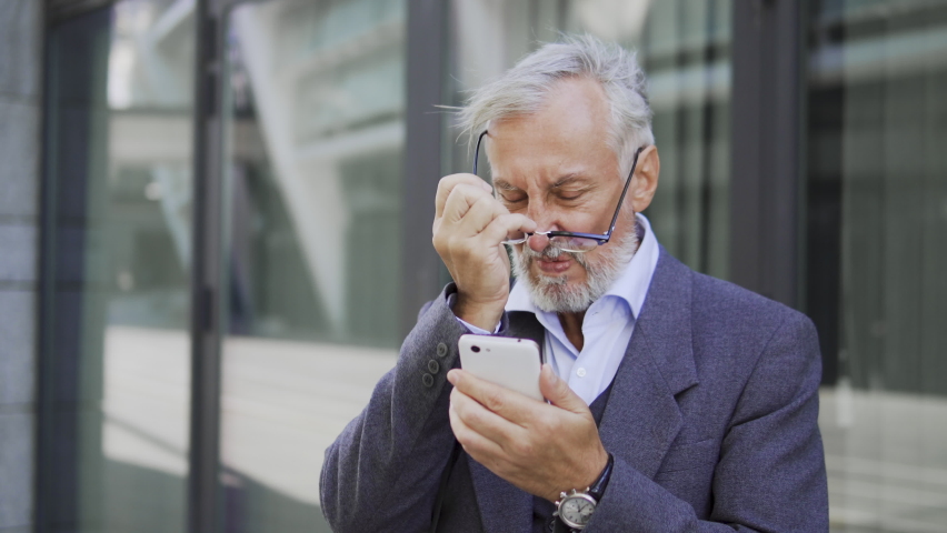 Adult businessman in eyeglasses looking at stocks rate in stock market app on his smartphone, becoming furious because of fall in price, losing money | Shutterstock HD Video #1086929330