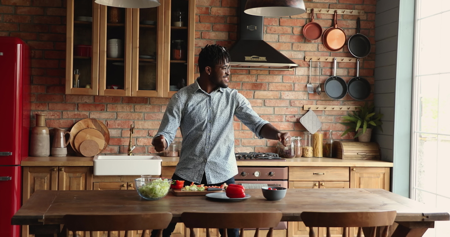 Energetic young Black hipster man homeowner enjoy dance in joyful disco rhythm at large modern home kitchen take break in preparing lunch. Active millennial guy vegan excited with cooking healthy food Royalty-Free Stock Footage #1086932930