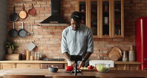 Charismatic young Black man food blogger hipster shoot culinary tutorial at home kitchen on smartphone. Enthusiastic millennial guy master chef record vlog webcast live teach to cook fresh vegan salad
