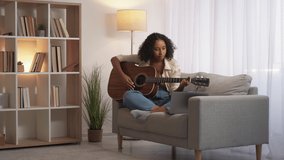 Music instrument practice. Guitar course. Chords learning. Cheerful woman guitarist studying online internet lesson on laptop on couch at home living room free space.