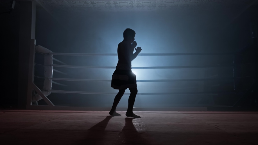 Silhouette of child kickboxer practicing shadow boxing in smoky gym. Muay thai fighter training. Strength and motivation. Sport concept. Full length in 4K, UHD Royalty-Free Stock Footage #1086936926