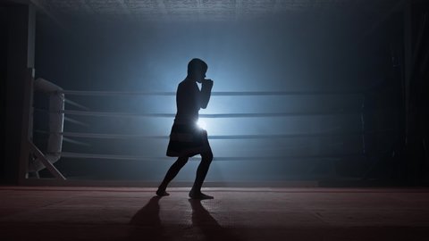 Silhouette of child kickboxer practicing shadow boxing in smoky gym. Muay thai fighter training. Strength and motivation. Sport concept. Full length in 4K, UHD