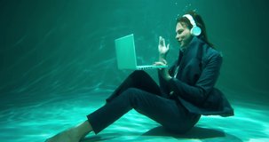 CUSTOMER SERVICE Young attractive business woman using laptop webcam video call, headphones under water slow motion.