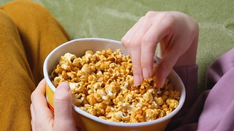 Close up view on female hand holding a popcorn while watching a movie in the living room.