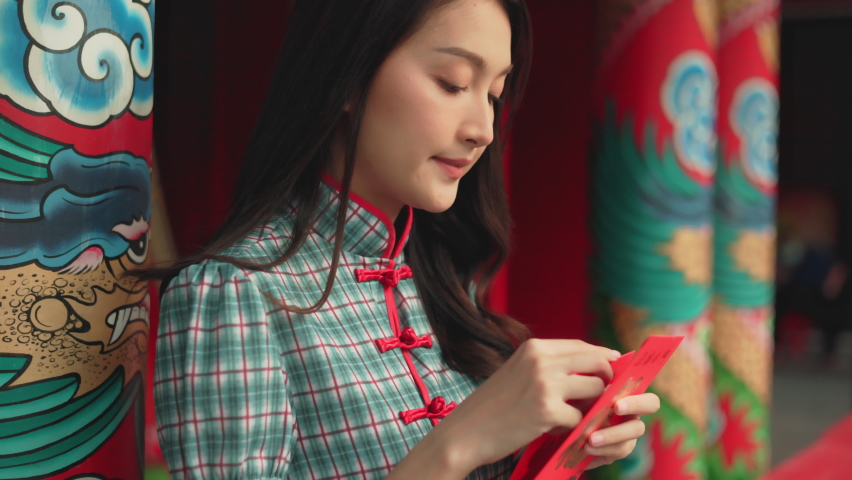 Beautiful Asian woman wearing a traditional red cheongsam on Chinese New Year.Hand holding red envelope or Ang pao with Chinese character means happiness or good fortune.