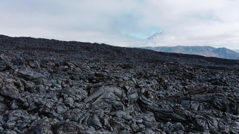 Black frozen lava flow from crater on the slopes of  Tolbachik volcanoes, on background Bolshaya Udina volcano, Kamchatka, Russia