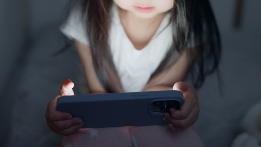 A four-year-old child looking at her phone in a dark room at night. Royalty-Free Stock Footage #1086951134