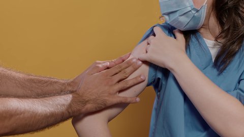 Closeup of medical doctor wearing surgical mask lifting sleeve and recieving band aid after covid or flu vaccine in studio. Detail view of medic getting bandage from male nurse after immunization.
