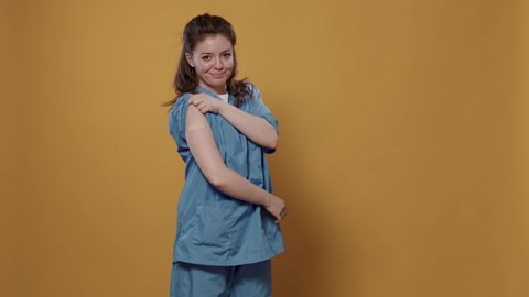 Portrait of confident medic lifting sleeve and showing band aid after covid or flu vaccine in studio. Smiling medical doctor in uniform revealing bandage covering immunization spot.