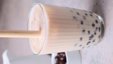 Milk bubble tea with tapioca pearls in glass, gray background.