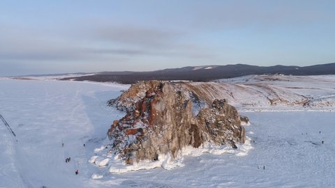 Aerial orbital shot of Shamanka rock and Cape Burkhan on Olkhon. Beautiful view on frozen Baikal. Panoramic winter landscape. Popular touristic destination