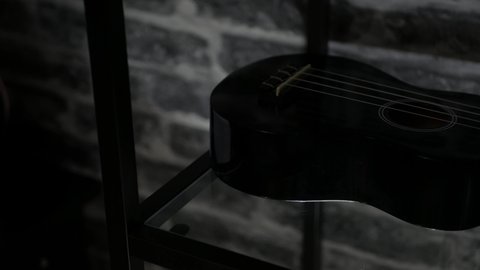 Black ukulele on a glass shelf infront of black brick wall