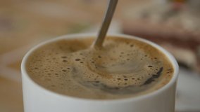 Fresh Morning Coffee Close Up. Slow Motion. Milk Hot Chocolate In White Cup. Man Stirs Sugar in Cup of Aromatic Coffee Closeup. Person Hand Stirring Cup Hot Chocolate.  - Powered by Shutterstock - Get 15% off with code: PIKWIZARD15