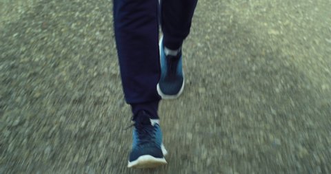 Cinematic close up shot of feet in sport shoes of athletic retired senior mature male runner in sportswear running with effort and dedication to maintain himself fit on countryside road at sunset.