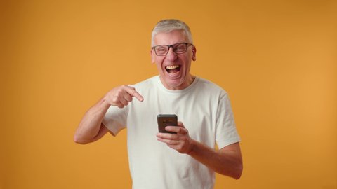 Elderly retired man looking at telephone screen, celebrating getting message with good news