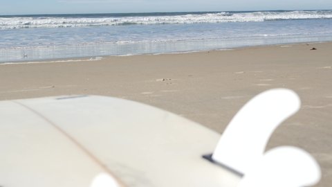 Surfboard for surfing lying on beach sand, California coast, USA. Ocean waves and white surf board or paddleboard. Longboard or sup for watersport recreation by sea water. Seamless looped cinemagraph.