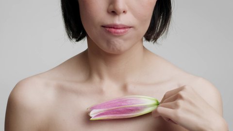 Unrecognizable Middle Aged Woman Stroking Neckline With Lily Flower On Gray Studio Background. Wellness And Spa, Bodycare And Natural Cosmetics Concept. Cropped Shot