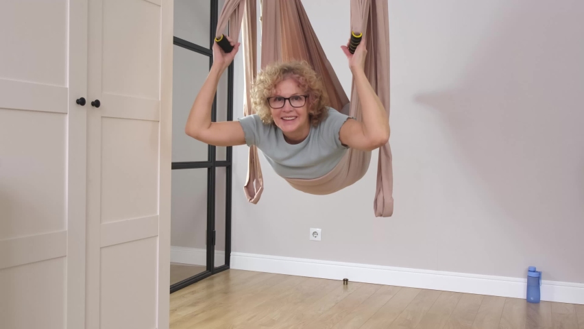 Senior beautiful sporty woman wearing glasses is doing exercises in the hammock