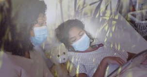 Animation of grass over biracial mother with face masks and her daughter lying in hospital. medical and healthcare services during pandemic concept digitally generated video.