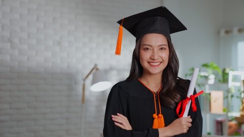 Slow motion indoors. Asian female graduate in a traditional clothes and cap smiling to the camera and holding her diploma smiles and congratulates her graduation on the university. Celebrating finish.