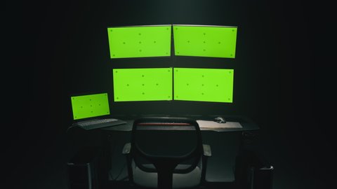 Zoom in view of computer monitors with chromakey green screens placed on table in dark ambient room of hacker base