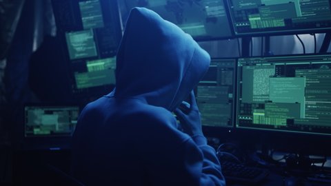Anonymous hacker in hoodie writing code and explaining attack to associate while hacking stock market in dark room
