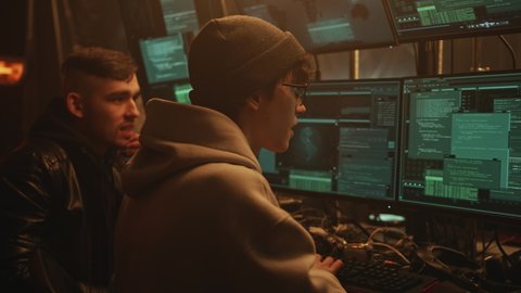 Excited software hackers in casual clothes making a cyber attack in a dark cybercriminals room with computers
