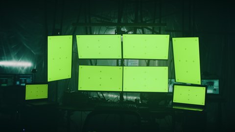 Zoom in view of hi tech computer multiple monitors and netbooks with green screens chromakey ready for hacker attack in dark room