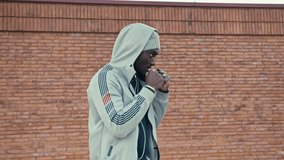 Athletic black man is boxing outdoor on a sunny day. He is wearing unbranded sports clothes and headphones. Brick wall and mountain landscape on the background. 4k slow motion video.