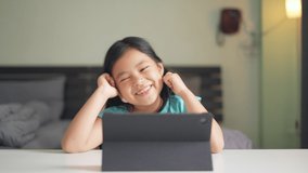 Asian child happy smile talking fun to teacher via video call learning on computer tablet or kid girl student enjoy touch screen and studying online class or person learn from home school in bedroom
