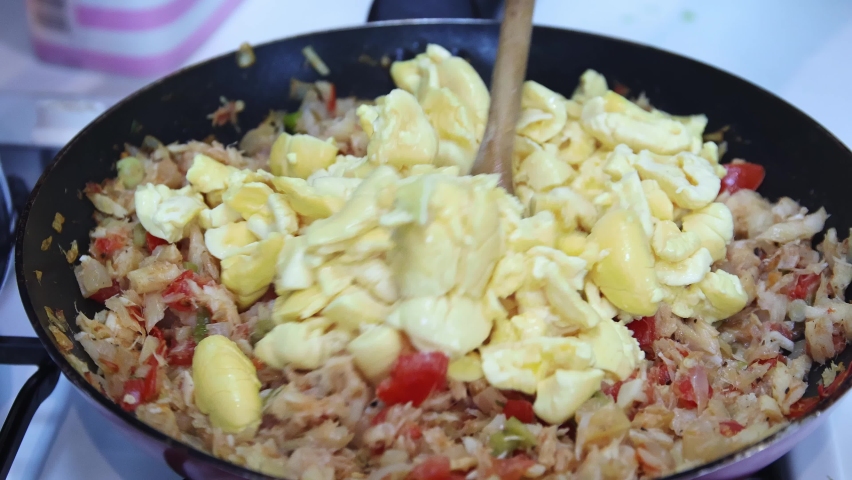 Ackee and saltfish, national dish of Jamaica.  Person of African ethnicity, stirring ackee into a pan of saltfish, tomatoes, onions, garlic, allspice, scotch bonnet peppers and thyme.  Slow motion. | Shutterstock HD Video #1086979118