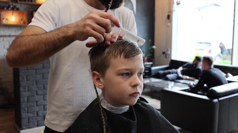 process of cutting a blond boy with a long braid in a chair in a barbershop salon, a barbershop concept for men and boys