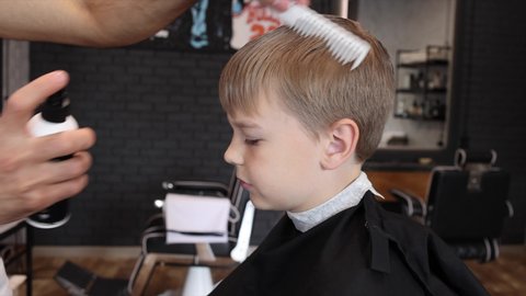 process of cutting a blond boy with a long braid in a chair in a barbershop salon, a barbershop concept for men and boys