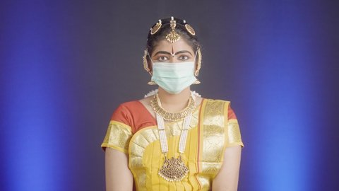 Bharatnatyam dancer with medical face mask turning by looking at camera - concpet of protection against covid-19 coronavirus infection and pollution