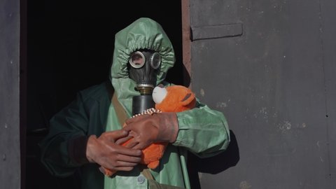 Person in protective clothes and gloves holds toy bear in hands. People care and healthcare during radioactive accident concept.