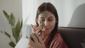 Happy Woman Applying Nourishing Cleansing Organic Clay Mask On Face, Looking At Mirror In Cozy Bedroom, Morning Routine. Beauty, Pampering, Home Spa Concept. Skin Care Cosmetic Concept Slow Motion - Powered by Shutterstock - Get 15% off with code: PIKWIZARD15